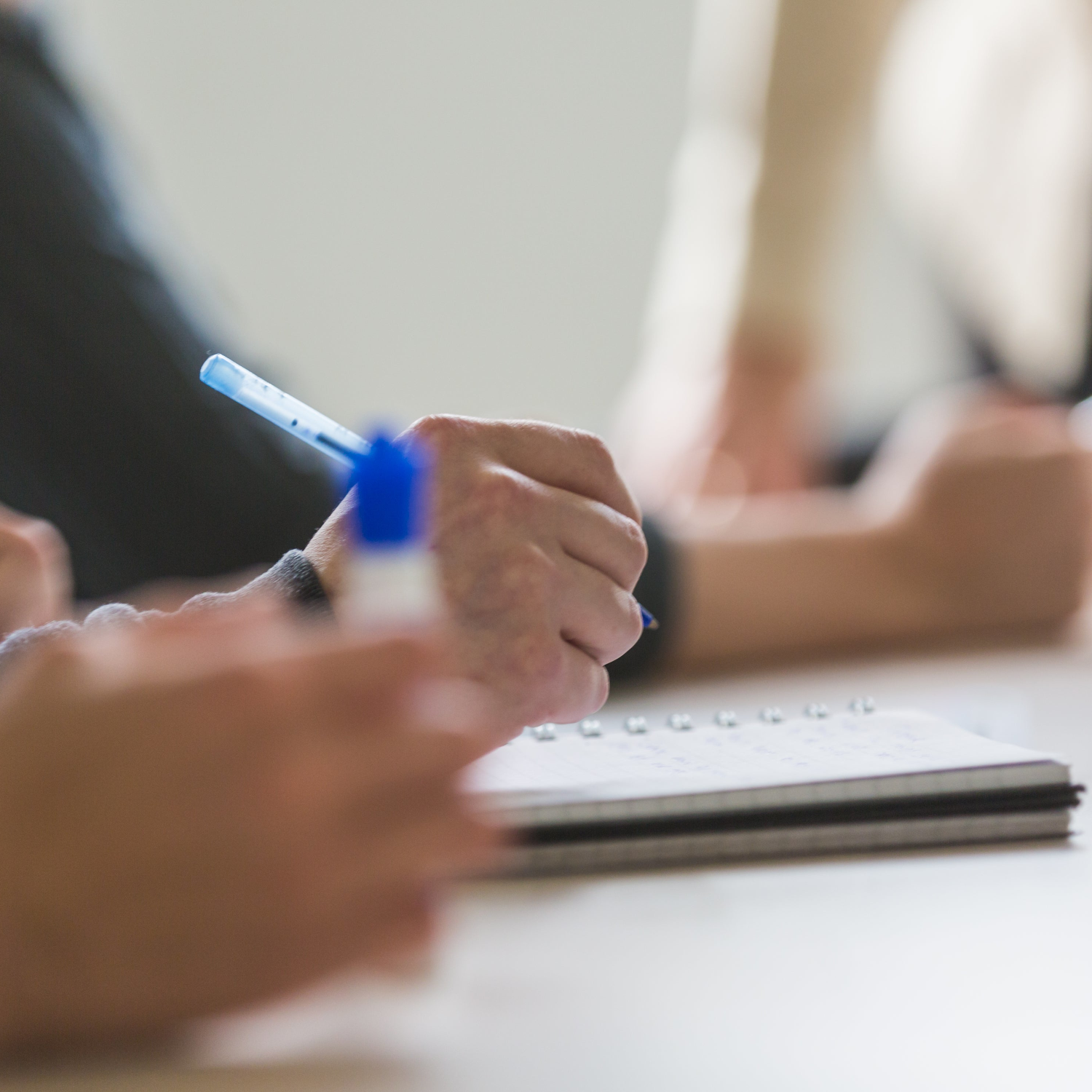 Meeting participants writing on notepads with pens at a table.