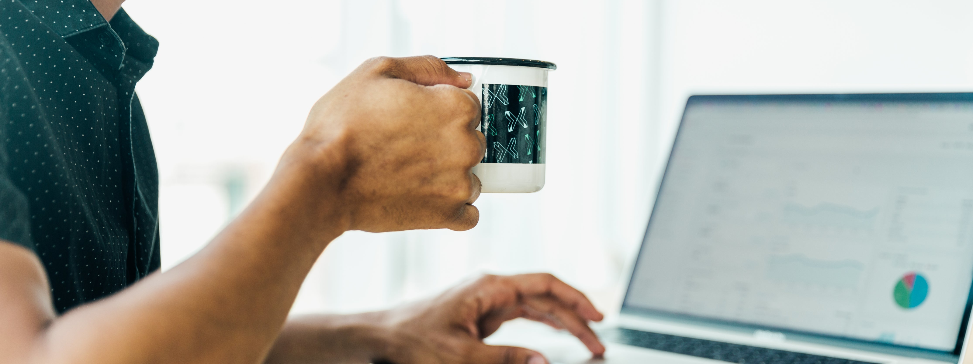 Person holding a mug with a laptop on a desk
