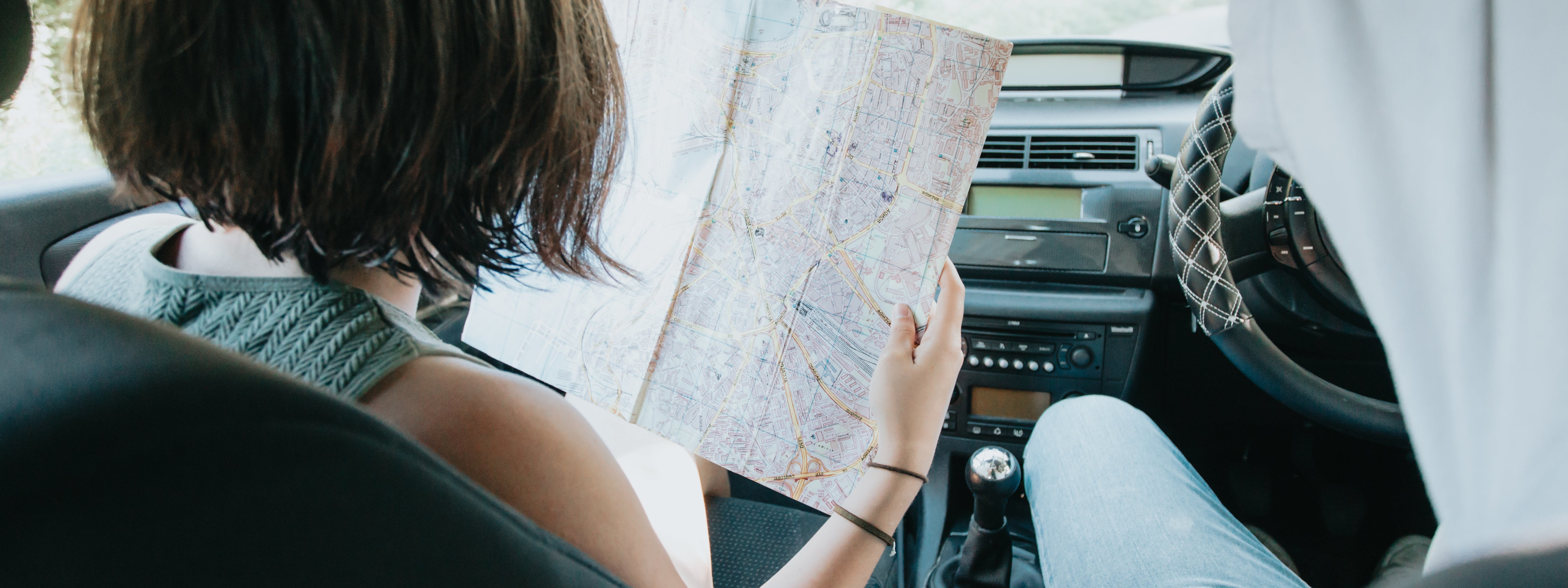 Two people in a car, one holding a map, with a focus on navigation.