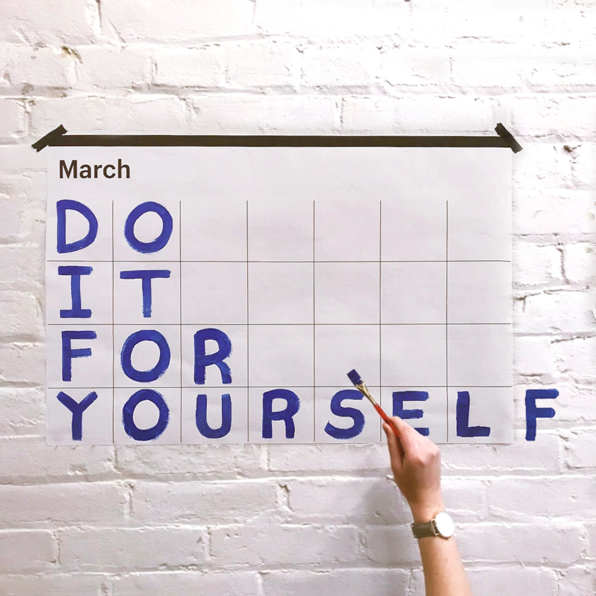 Calendar with 'DO IT FOR YOURSELF' text on a white brick wall
