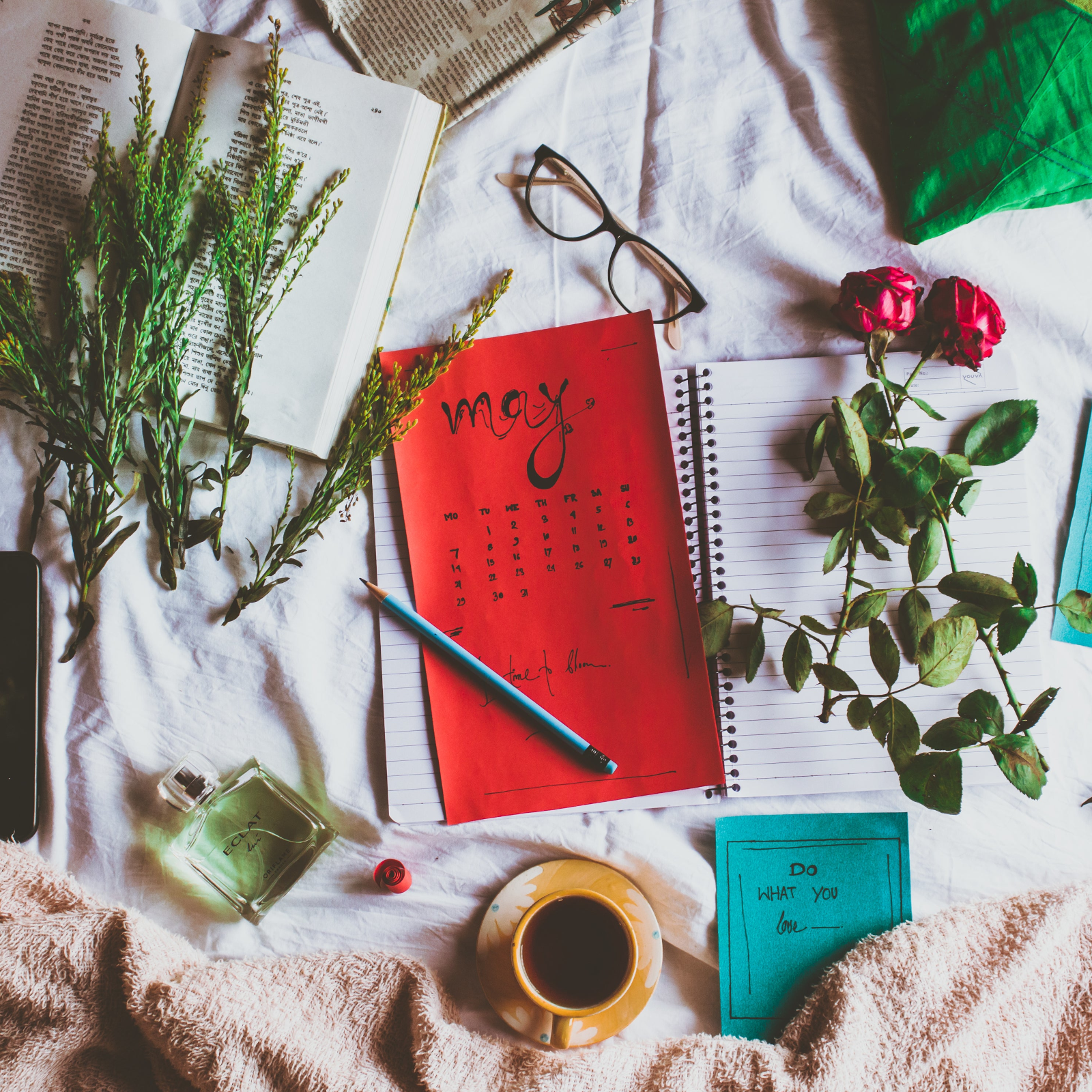 Calendar with 'May' on a tablecloth surrounded by flowers, a pencil, and a cup.